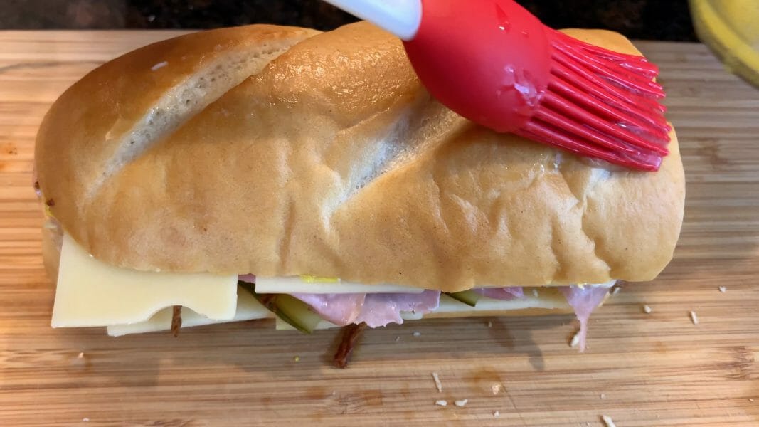 spreading melted butter on the Cuban sandwich