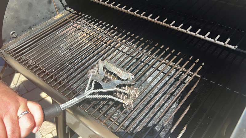 cleaning grill grates of Z Grills wood pellet grill with a cleaning brush