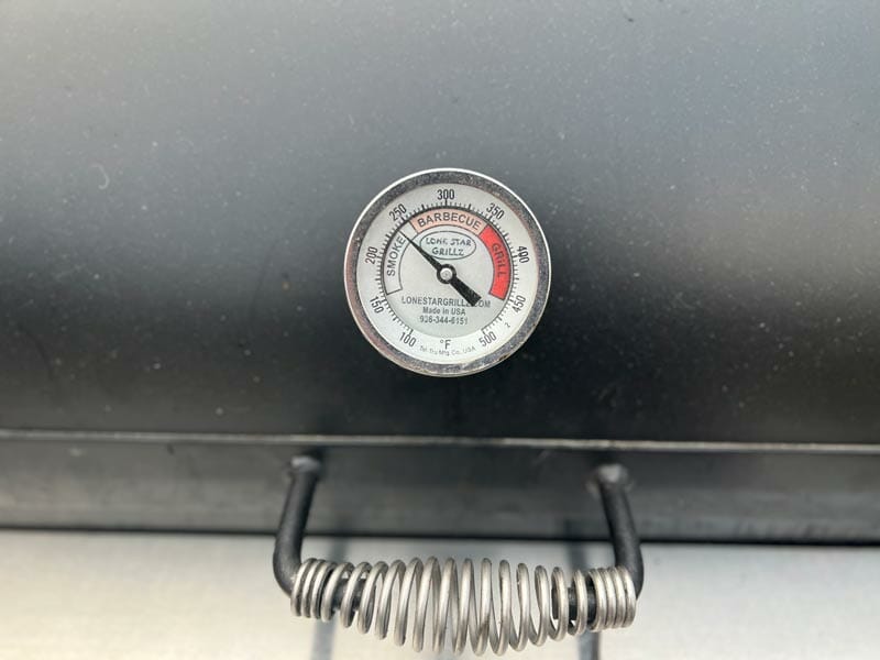 thermometer showing the smoker has nearly reached optimal cooking temperature to smoke chicken breast 