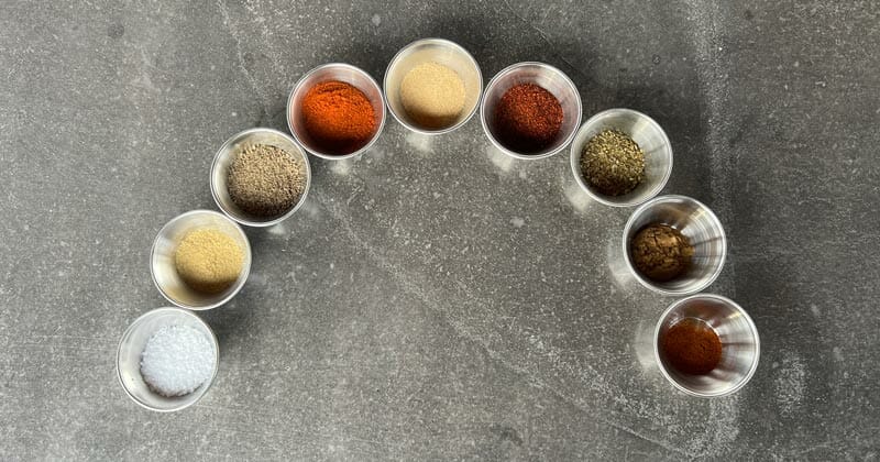 chicken rub ingredients including salt, seasoned salt, black pepper, garlic powder, oregano, ground cumin, chili powder, cayenne, smoked paprika