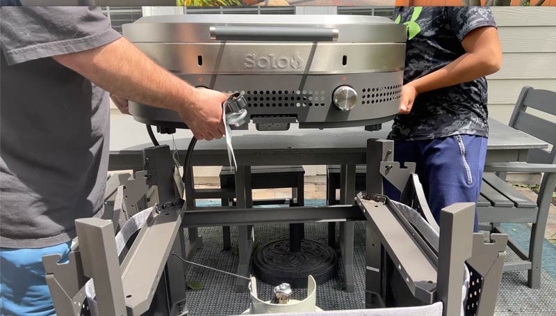 portable Solo Stove Steelfire griddle being lifted off the cart and placed on a table